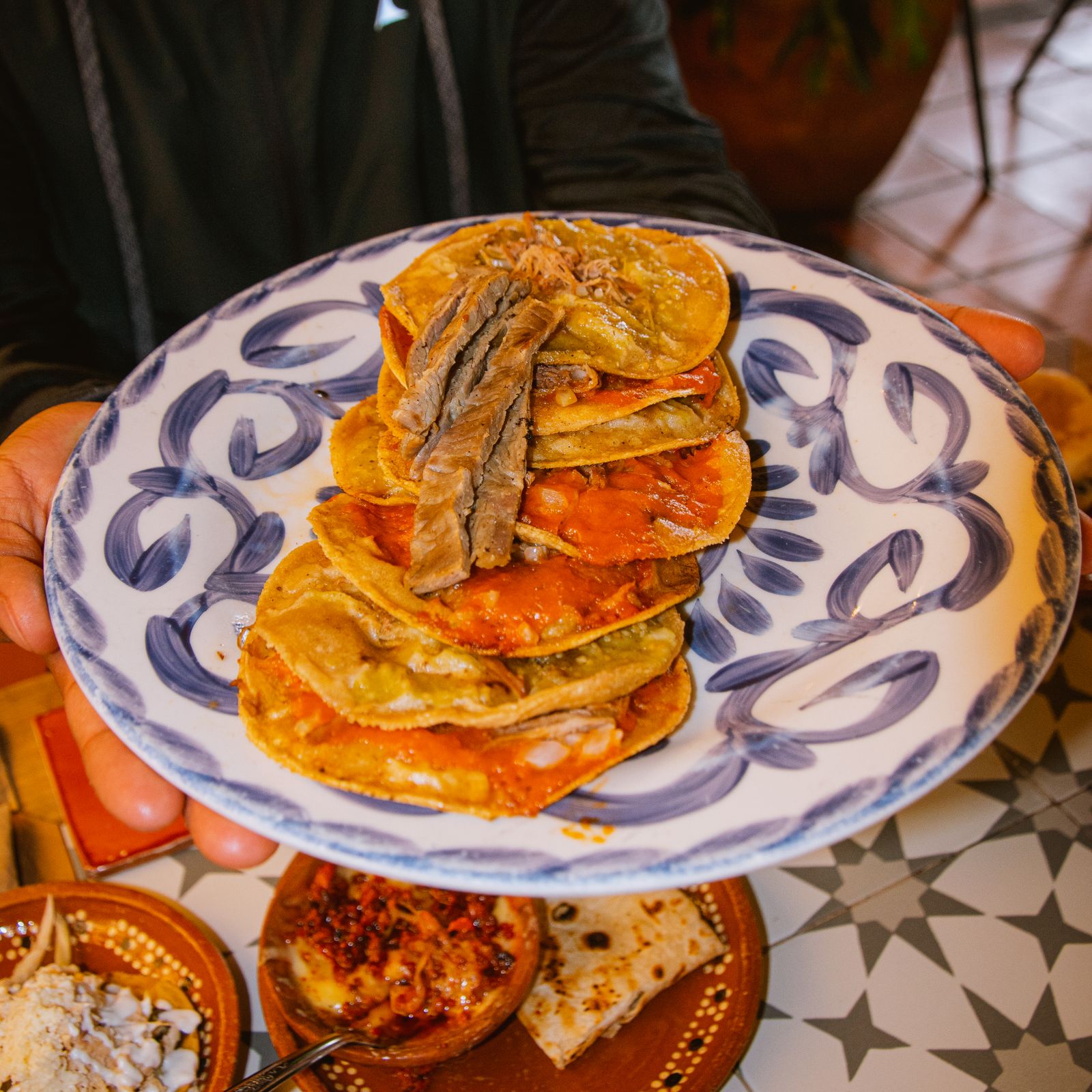 Stack of chile-red birria tacos on a hand-painted plate
