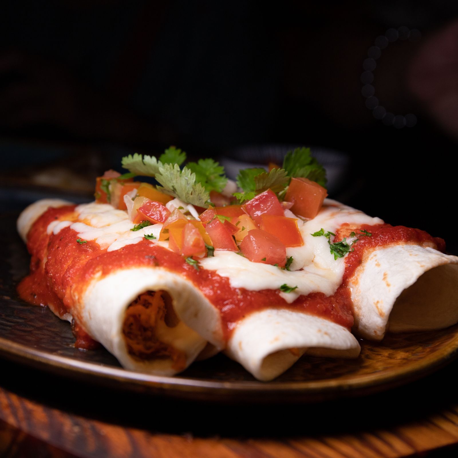 Enchiladas with red sauce, crema and cilantro on a green plate