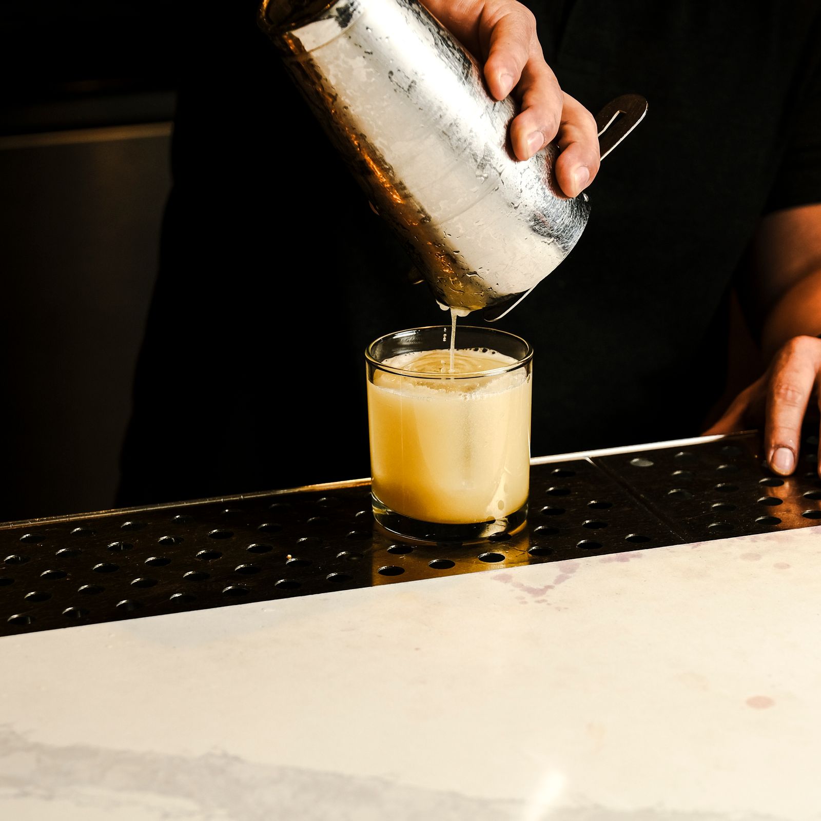 Bartender straining a freshly shaken cocktail into a glass
