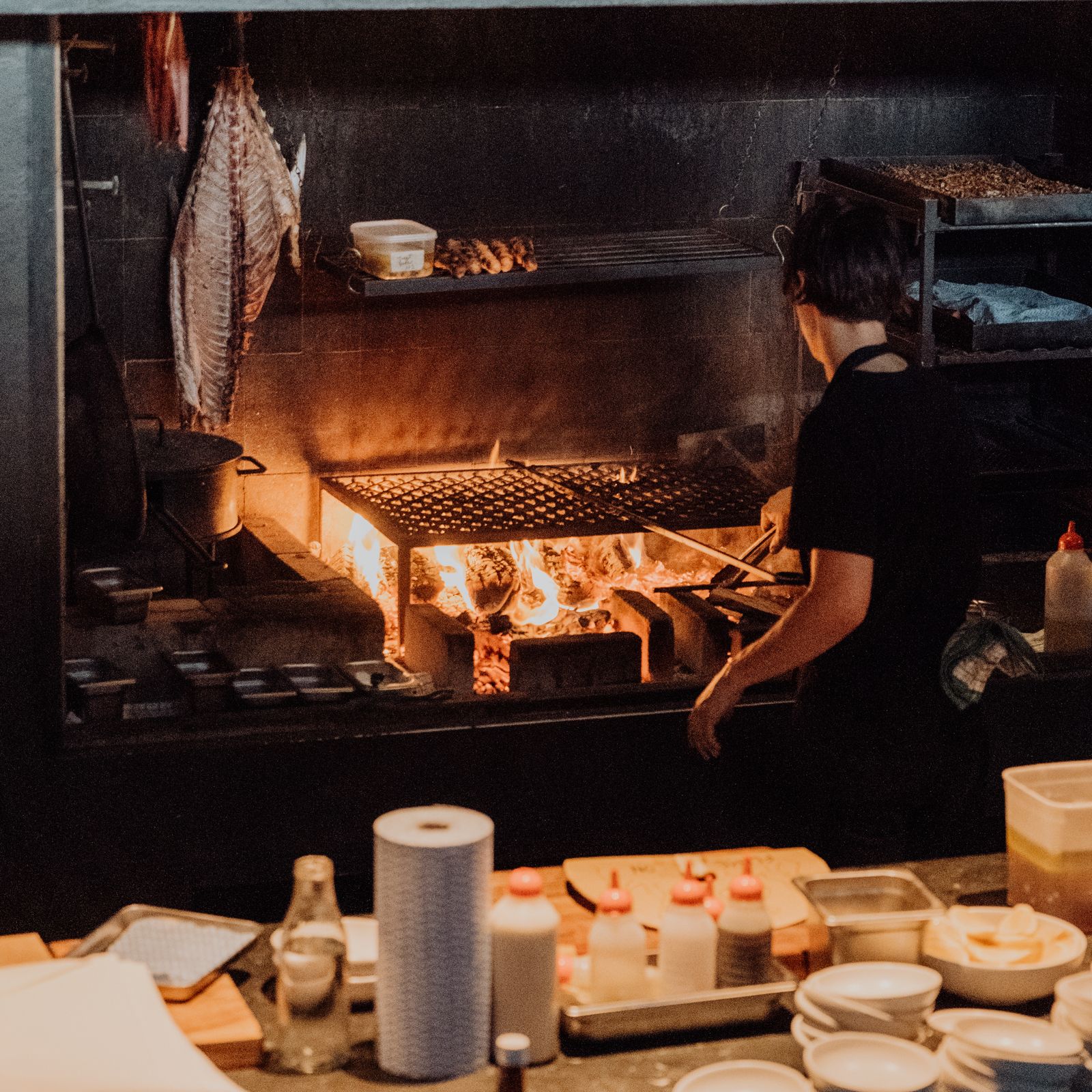 Cook working the wood-fired grill in the open kitchen